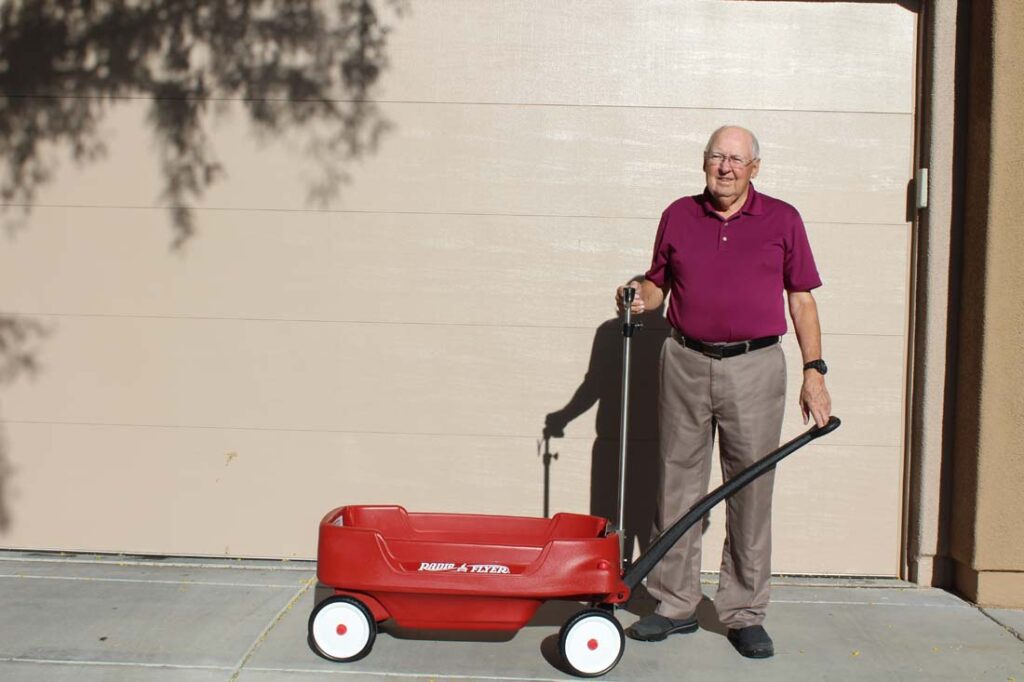 An old man holding a red wagon